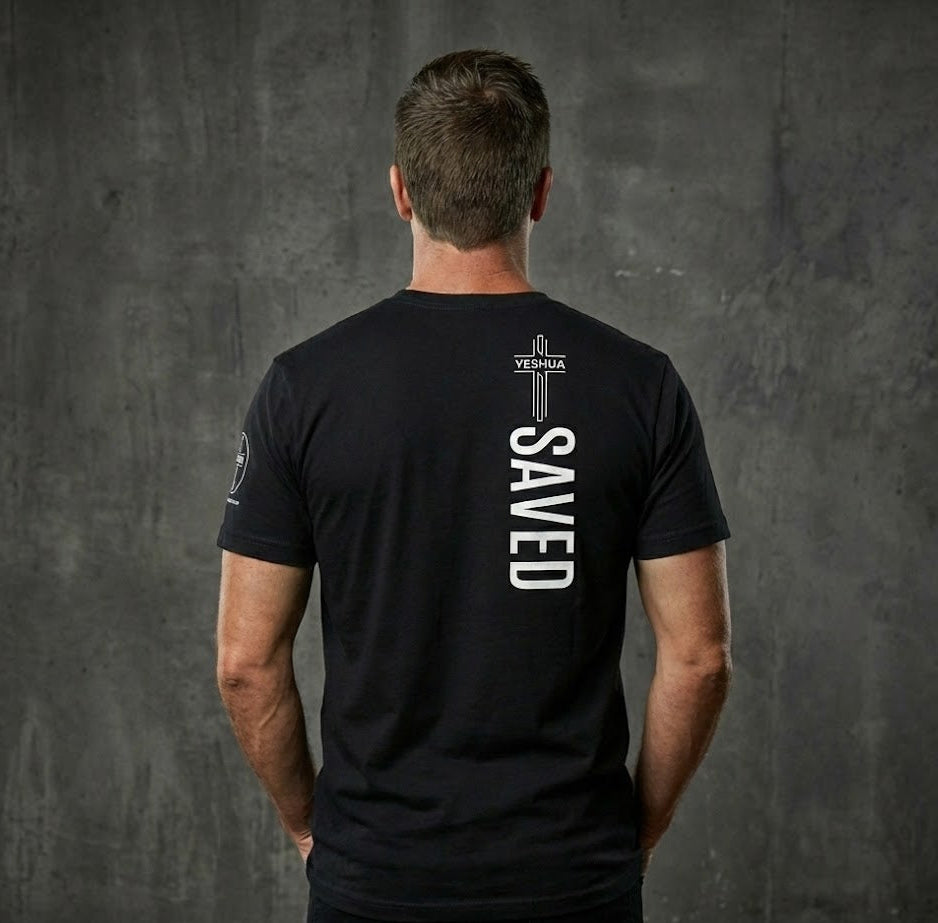 Man wearing a black t-shirt with 'SAVED' printed on the back against a gray wall.